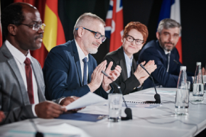 Group of people applauding speech of their colleague while sitting at table during conference